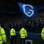 Sfeershot van een stadionvak met Genk-aanhang tijdens een Europese verplaatsing, met zicht op stewards en politie op de achtergrond.