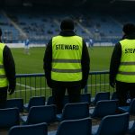 Sfeerbeeld in een stadion met tribune en stewards, zonder herkenbare gezichten