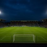 Voetbalstadion bij avond met verlichte tribunes en speelveld
