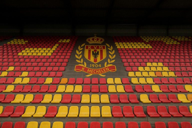 Stadion van KV Mechelen met tribunes in clubkleuren onder het licht