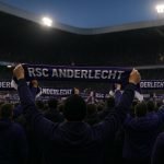 Supporters van Anderlecht met sjaals, gezien van achteren in het stadion bij schemerlicht