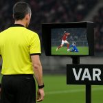 Een scheidsrechter met VAR-icoon op het scherm tijdens een wedstrijd, als illustratie bij de nieuwe IFAB-regels richting WK 2026.