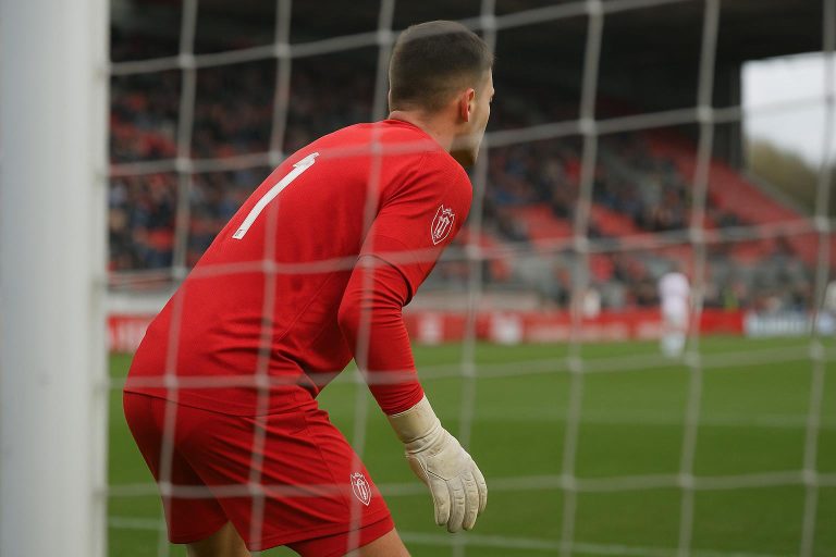 Een doelman van Standard Luik warmt op in het stadion met handschoenen, met het doel op de achtergrond.