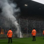 Beveiliging en supporters in een voetbalstadion met rook van pyrotechniek