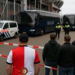 Politie en stewards bij de bezoekersbussen aan De Galgenwaard tijdens een uitmatch van Feyenoord, met supporters op afstand.