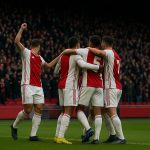 Spelers van Ajax vieren een doelpunt in het stadion, met supporters op de achtergrond.