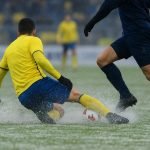 Spekglad voetbalveld tijdens STVV tegen Zulte Waregem, met spelers op afstand in winterse omstandigheden