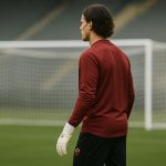 Doelman Mile Svilar van AS Roma op het trainingsveld, met handschoenen en doelnet op de achtergrond.