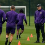 Beeld van de zijlijn bij RSC Anderlecht tijdens een trainingsmoment, met staf en spelers op de achtergrond.