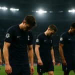 Spelers van Tottenham Hotspur druipen ontgoocheld af in een stadionomgeving bij avondlicht.