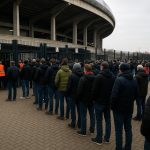 Supporters aan de ingang van een groot stadion met wachtrijen voor tickets