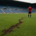 Zicht op een stuk grasmat in een stadionomgeving na vandalisme, zonder herkenbare personen.
