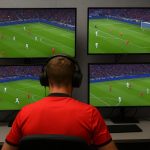 Een neutrale foto van een VAR-omgeving in een stadion, met schermen en een scheidsrechter in beeld zonder herkenbare gezichten.