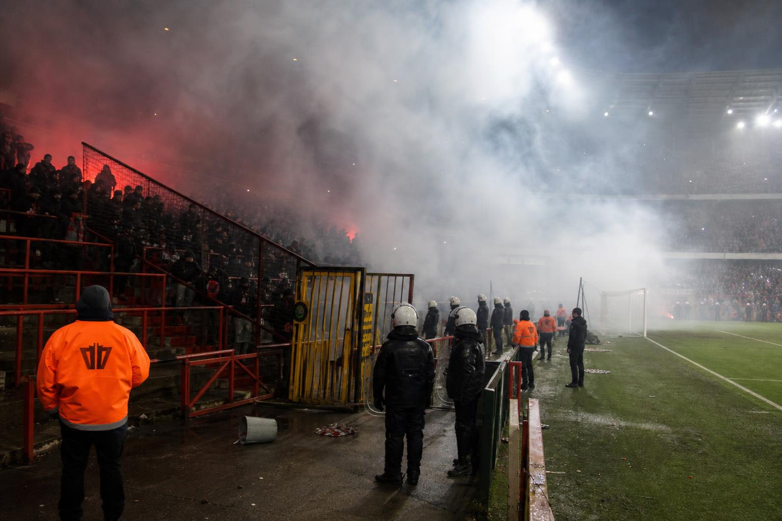 Gespannen supporterssfeer in een Belgisch voetbalstadion met rook op de tribunes