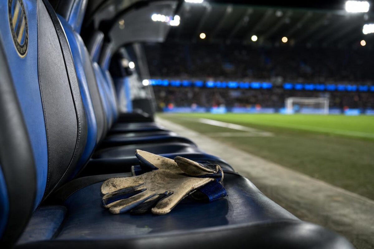 Doelmanshandschoenen op een lege bank in een blauw-zwarte stadionomgeving
