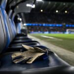 Doelmanshandschoenen op een lege bank in een blauw-zwarte stadionomgeving