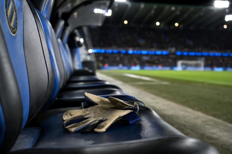 Doelmanshandschoenen op een lege bank in een blauw-zwarte stadionomgeving