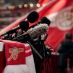 Arsenal-sfeer met persmicrofoons en stadionlichten rond het voetbalverleden van Remco Evenepoel
