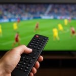 Sfeerbeeld van een tv-scherm met voetbaluitzending in een woonkamer, zonder herkenbare gezichten