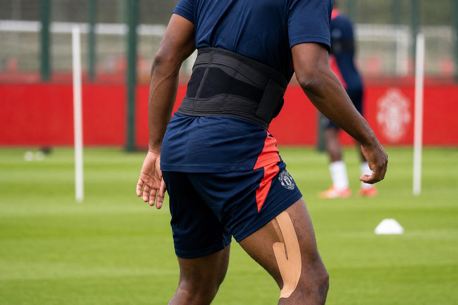 Sfeerbeeld van een speler in Manchester United-trainingskledij tijdens een revalidatiemoment op het oefenveld