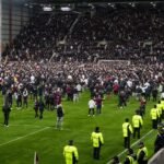 Supporters op het veld in Celtic Park na het titelduel, met spelers op de achtergrond.