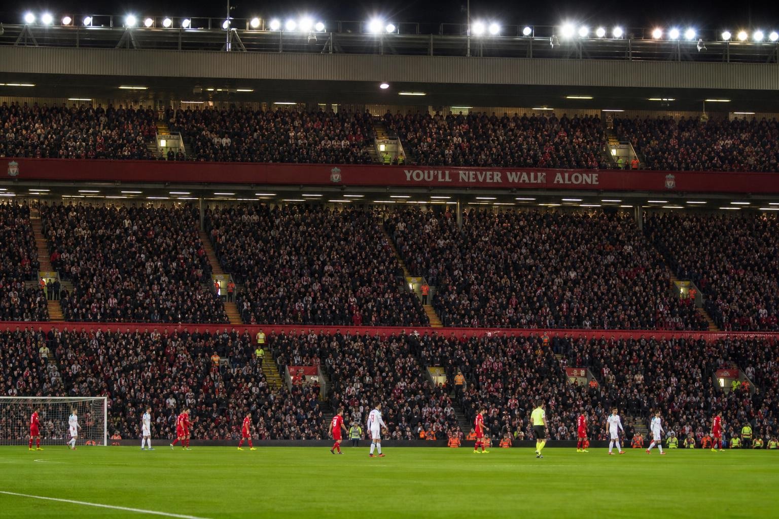 Sfeershot in en rond Anfield met gespannen wedstrijdcontext, zonder herkenbare gezichten.
