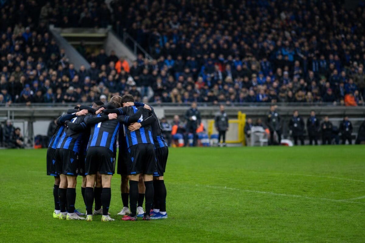 Spelers van Club Brugge vieren samen op het veld na een wedstrijd, met het stadion op de achtergrond.