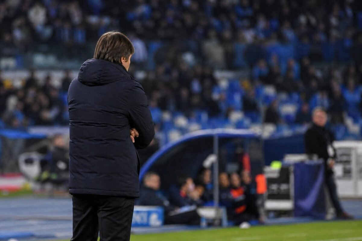 Antonio Conte aan de zijlijn bij Napoli tijdens een wedstrijd, met stadionlichten op de achtergrond