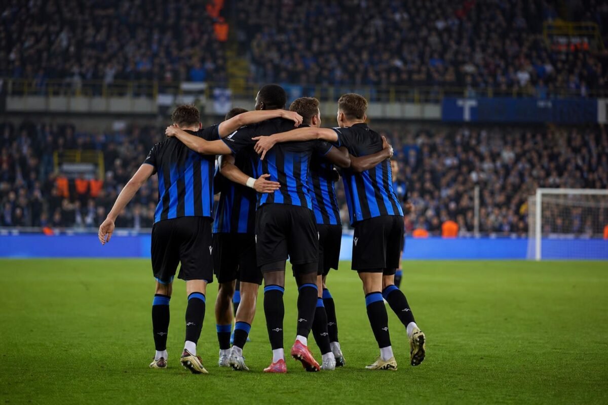 Spelers van Club Brugge vieren een goal tijdens een wedstrijd, met het stadion op de achtergrond.