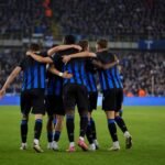 Spelers van Club Brugge vieren een goal tijdens een wedstrijd, met het stadion op de achtergrond.