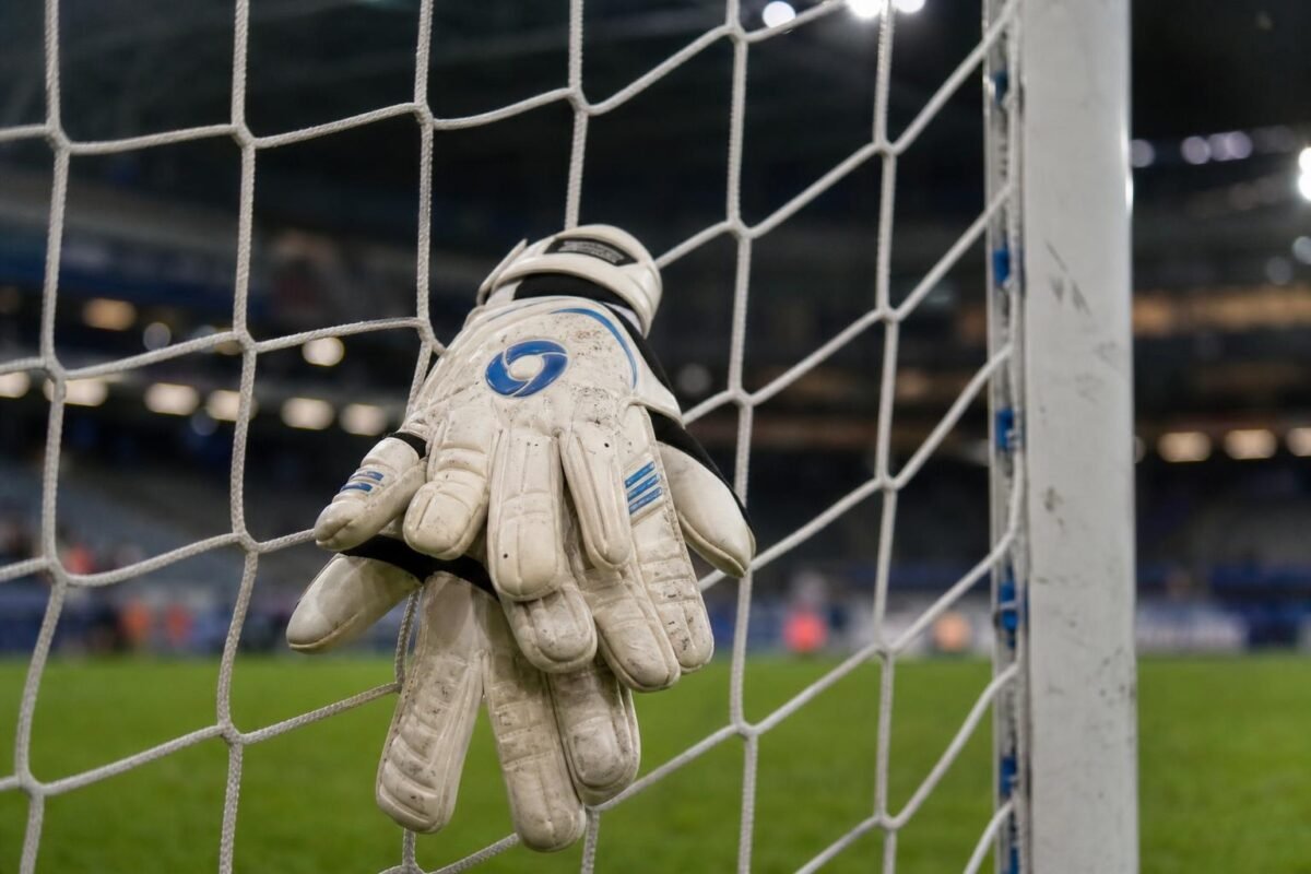 Keepershandschoenen aan een doelnet in een gespannen KAA Gent-sfeer.