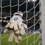 Keepershandschoenen aan een doelnet in een gespannen KAA Gent-sfeer.