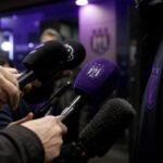 Gespannen persomgeving rond Anderlecht met microfoons en paars-zwarte sfeer zonder herkenbare personen