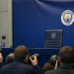 Een persmoment in Manchester City-sfeer met lege trainersstoel en camera’s rond de verwachte komst van Enzo Maresca.