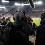 Televisiecamera’s en persmicrofoons langs een voetbalveld na een beladen wedstrijd