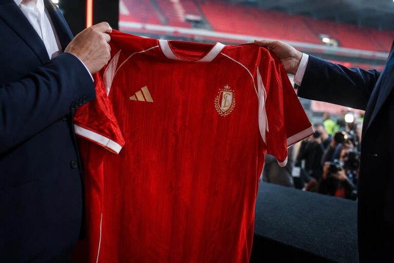 Een rood Standard Luik-thuisshirt wordt gepresenteerd in een clubcontext zonder herkenbare gezichten.