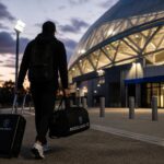 Transferachtige stadionomgeving met voetbaltas en valiezen onder de stadionlichten