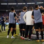 Een hydration break langs de zijlijn tijdens een voetbalwedstrijd met tv-camera’s op de achtergrond