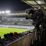 Televisiecamera's en persmateriaal in een Belgisch voetbalstadion tijdens een gespannen rechtenconflict