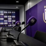 Persmoment in een Anderlecht-context met microfoons en paars-witte voetbalsetting