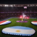 WK-stadion met grote nationale vlaggen en spelersgroepen rond de middencirkel voor de aftrap