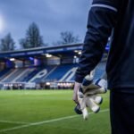 Transferbeeld rond Patro Eisden met doelmannenhandschoenen in een stadioncontext