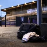 Keepershandschoenen en sporttas in een transfercontext bij een voetbalstadion.
