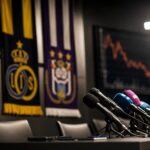 Microfoons in een Belgische voetbalpersruimte bij een debat over de financiële rol van transfers.
