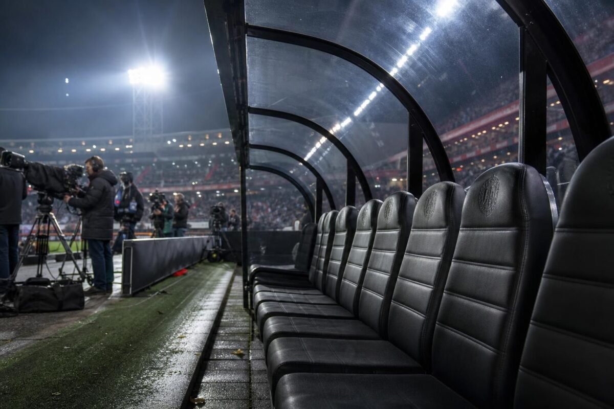 Gespannen voetbalsfeer rond een trainerszoektocht in een stadion zonder herkenbare gezichten