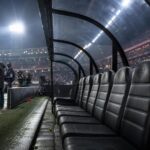 Gespannen voetbalsfeer rond een trainerszoektocht in een stadion zonder herkenbare gezichten