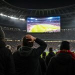 Supporters kijken voor de aftrap naar een groot stadionscherm in een WK-stadion.