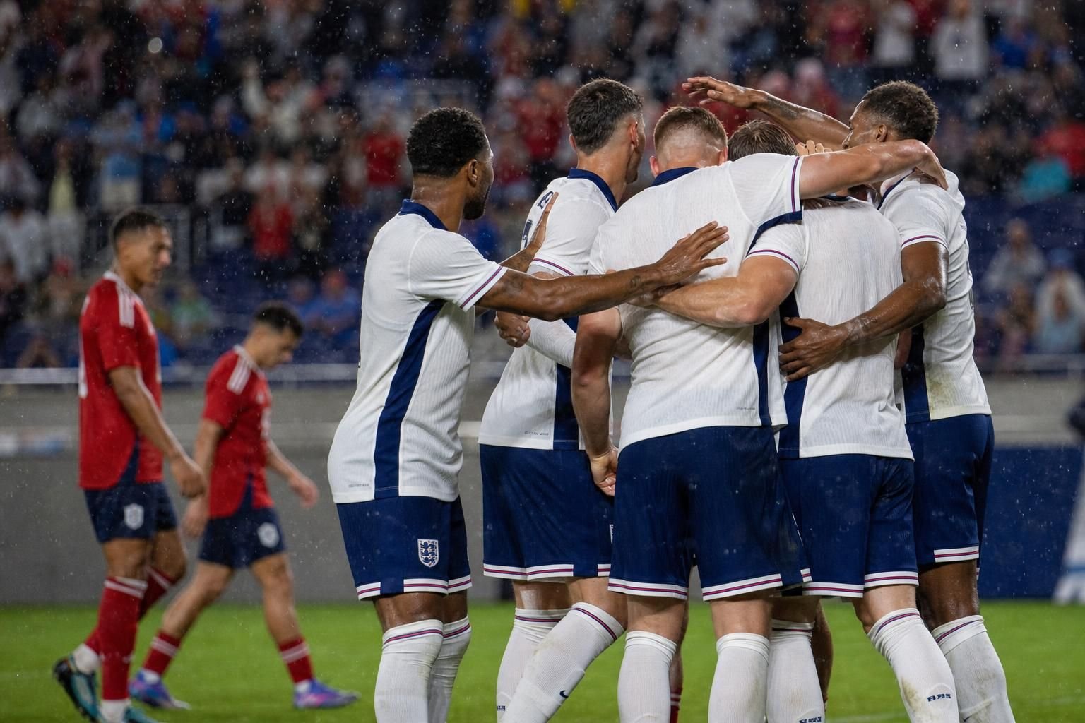 Engelse spelers vieren vanop afstand een doelpunt in een regenachtige oefeninterland tegen Costa Rica