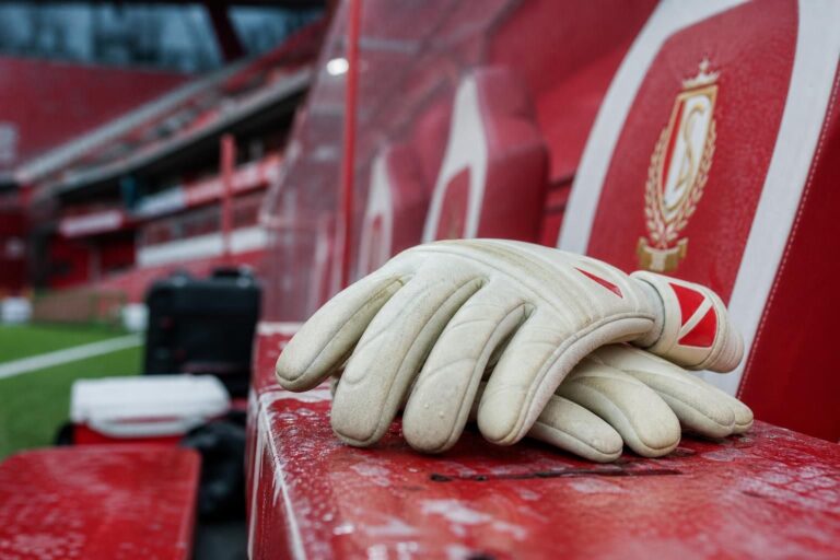 Transfercontext rond Standard Luik met keepershandschoenen en rood-witte stadiondetails zonder herkenbare gezichten