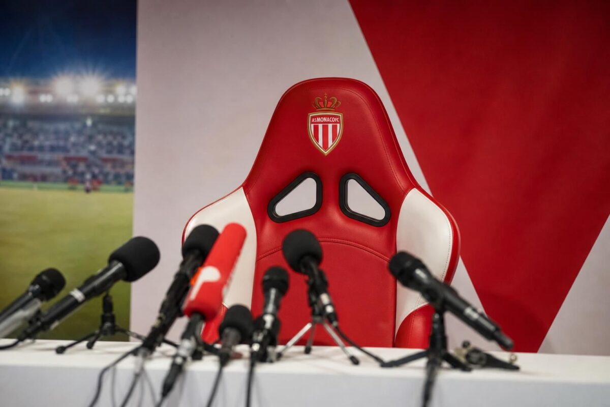 Persruimte in AS Monaco-sfeer met lege trainersstoel en microfoons rond een mogelijke trainersaanstelling